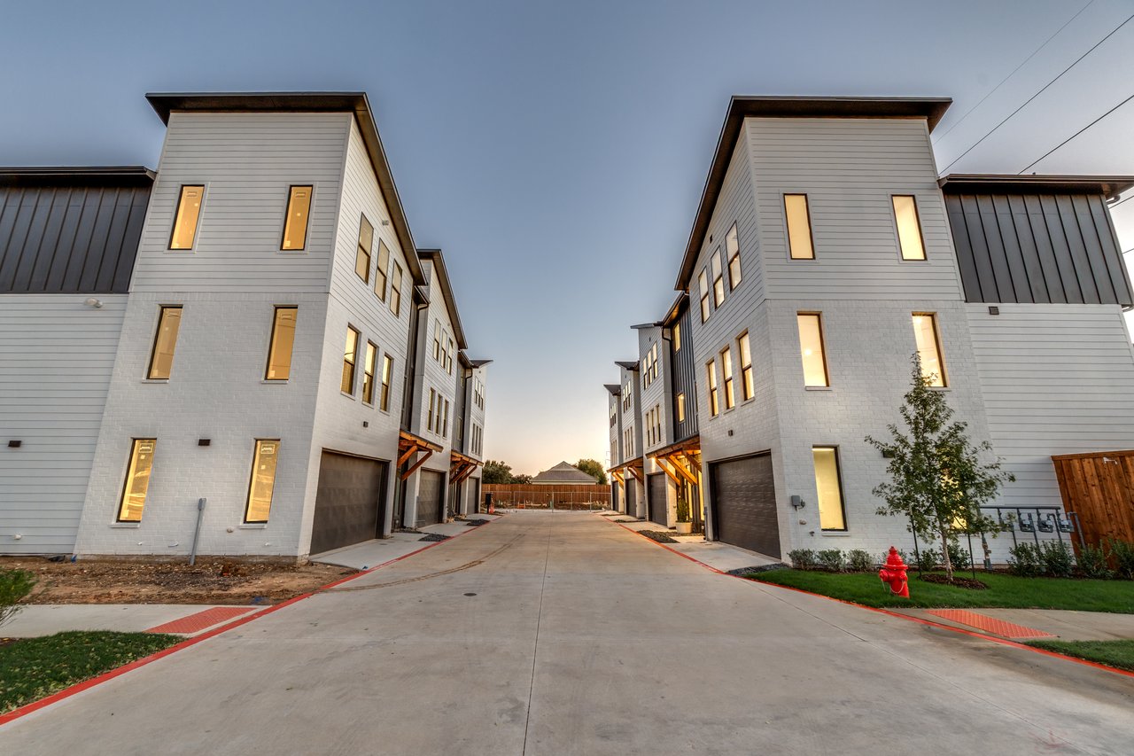 Modern townhomes line a central driveway, with dark metal accents and warmly lit windows.