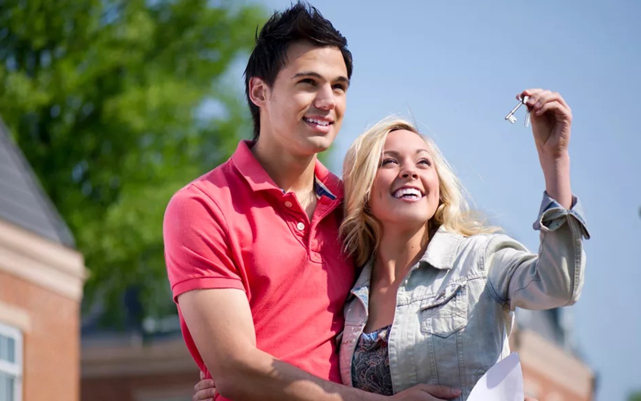A smiling couple celebrates outside a house as the woman raises their new keys.