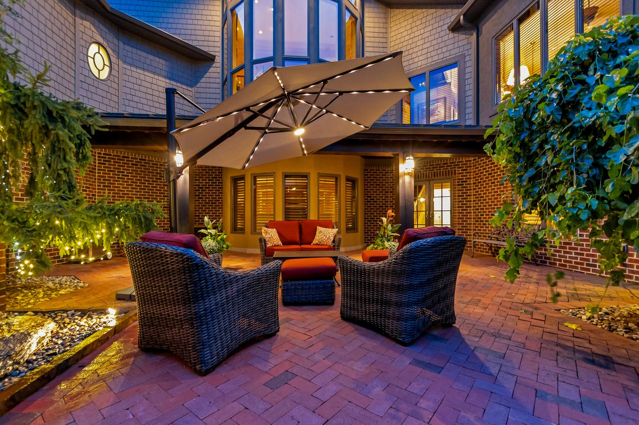 Outdoor patio with wicker lounge seating beneath a large umbrella, illuminated at night.