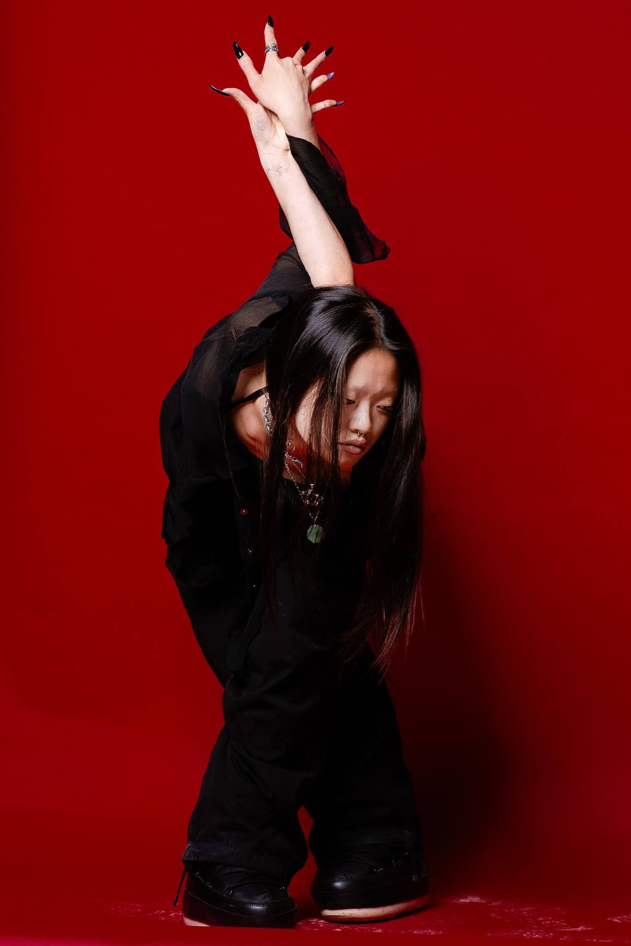 Dancer in black bends forward with one arm raised against a vivid red backdrop.