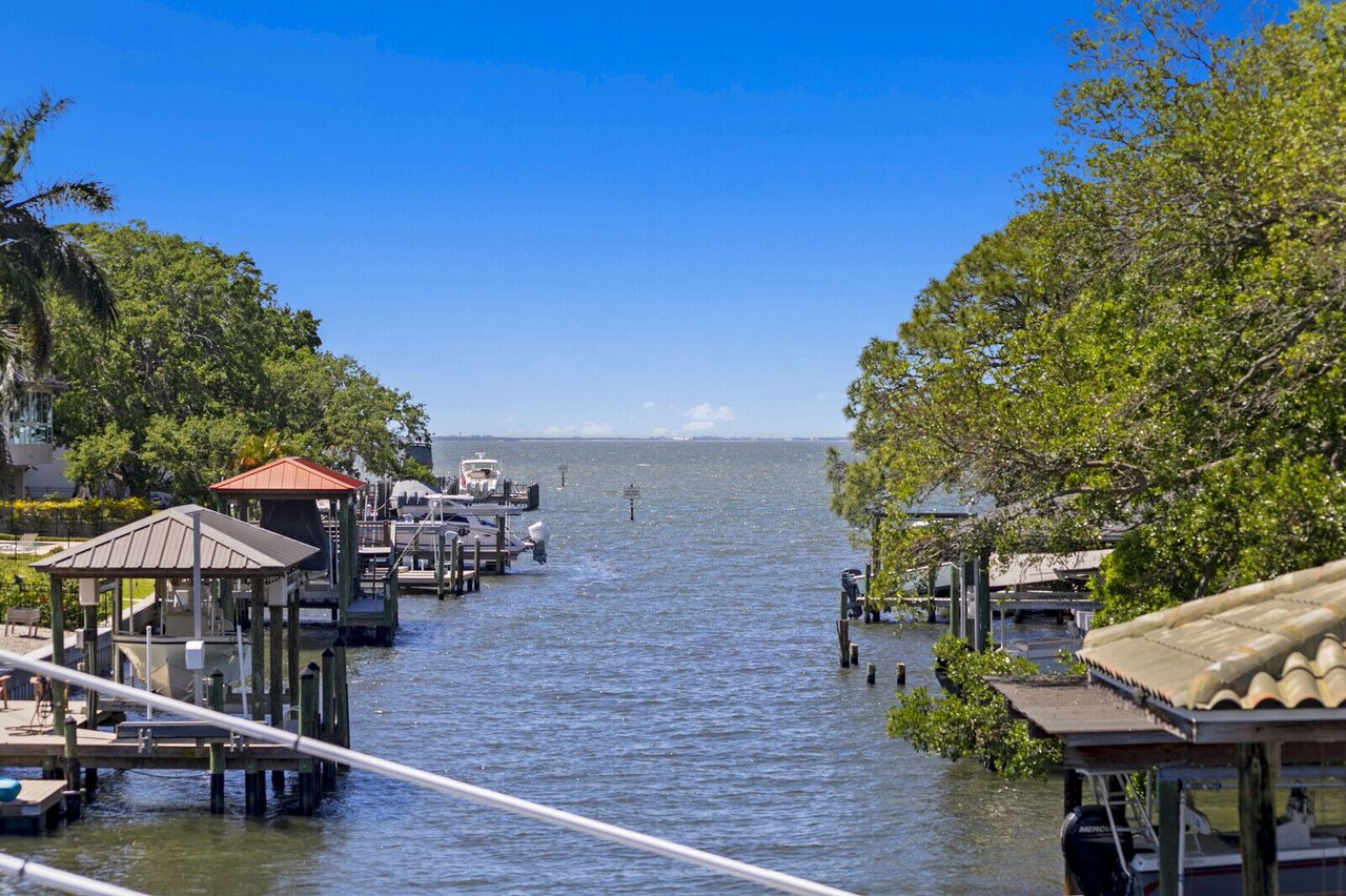 Tree-lined waterfront channel with covered docks and boats along the shore.