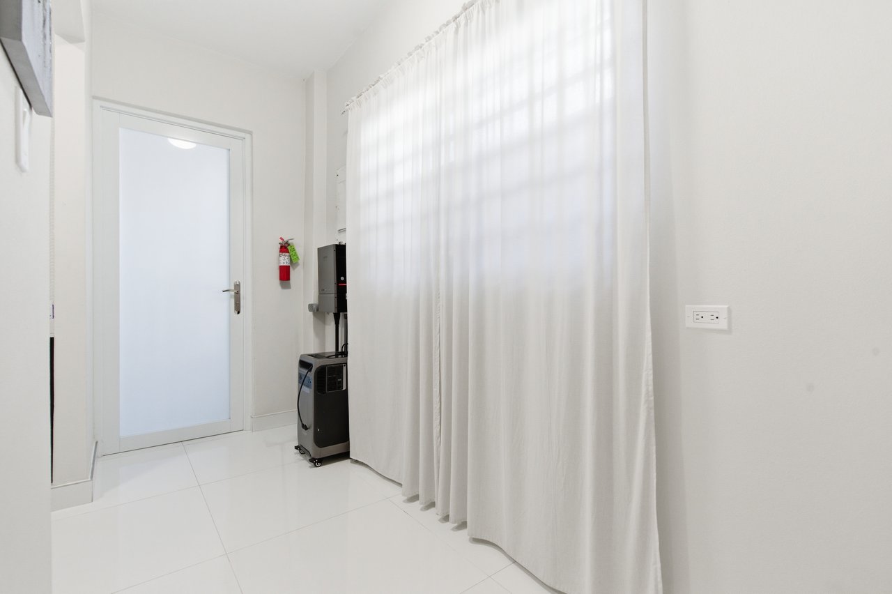 White-tiled interior with a frosted-glass door, floor-length curtains, and a compact black appliance.