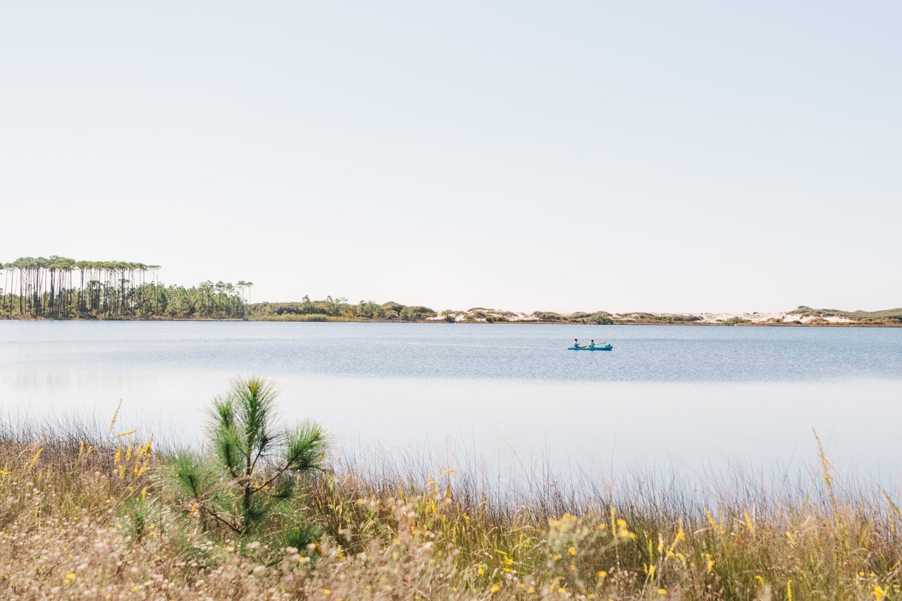A canoe drifting across the glassy tea-colored water of WaterColor's Western Lake framed by golden dune grasses on 30A, Florida