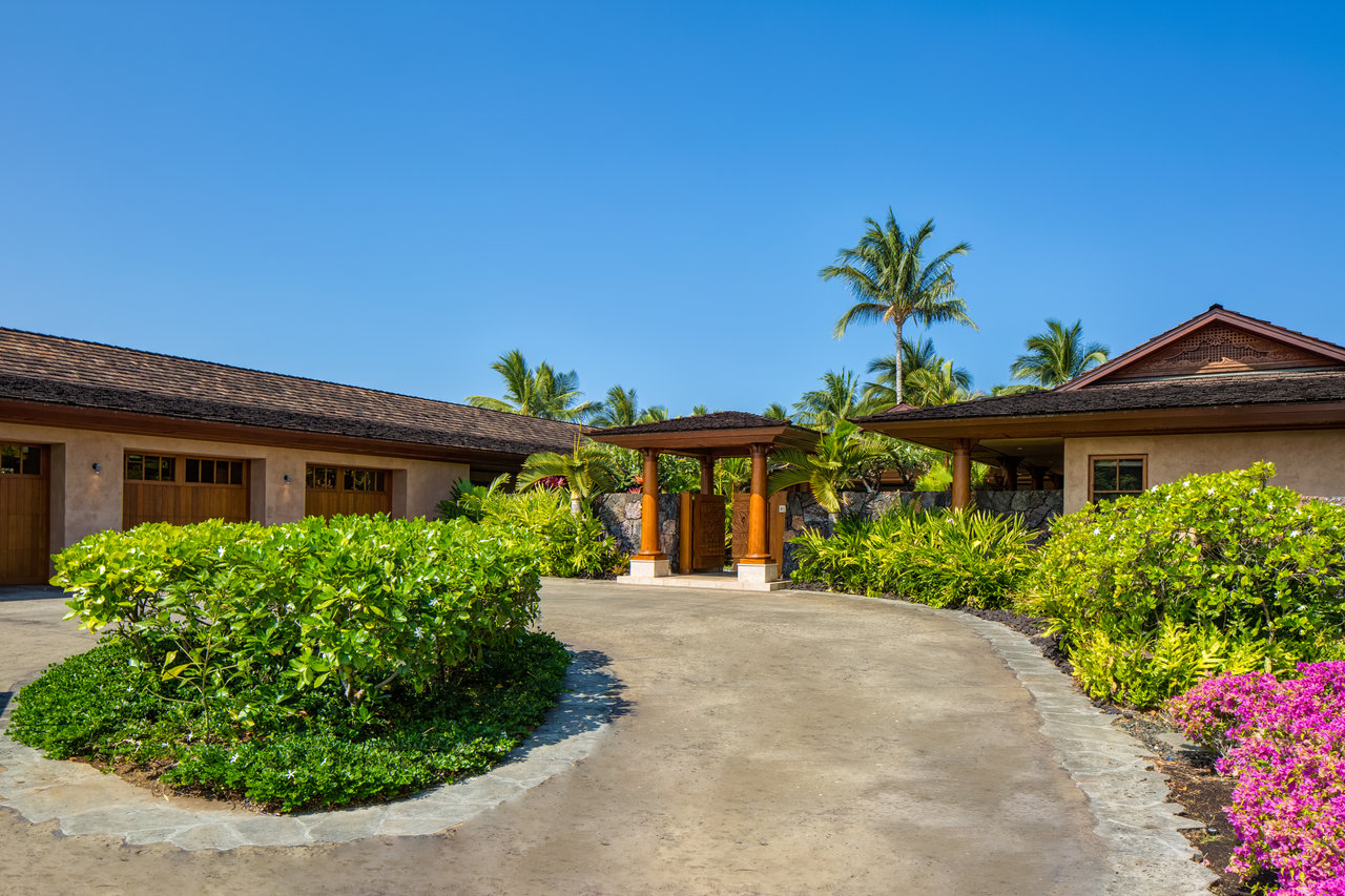Home entrance with a curved driveway, tropical palms, and colorful flowering shrubs.