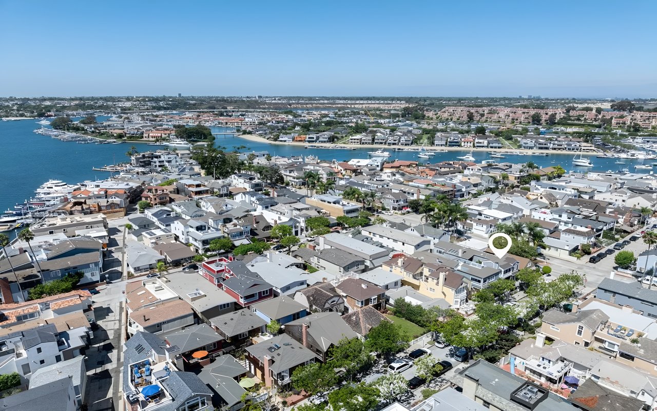  An aerial view of a crowded residential neighborhood with a white pin marking a house, with a marina and bay in the background.