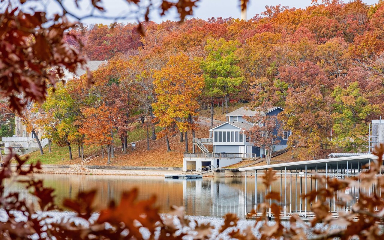 Waterfront homes and docks beside a calm lake, framed by colorful autumn foliage.