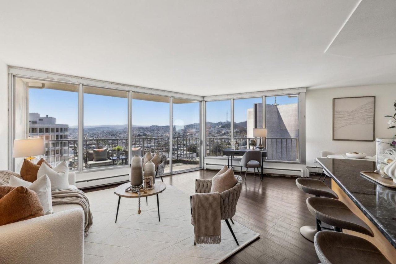 Furnished high-rise living room with floor-to-ceiling corner windows overlooking the city and hills.