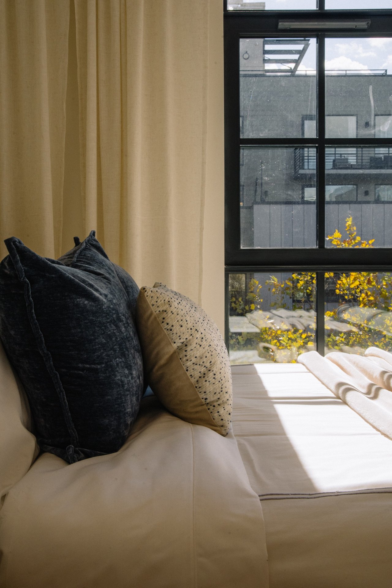 Furnished window seat with layered pillows beside large windows overlooking autumn foliage.