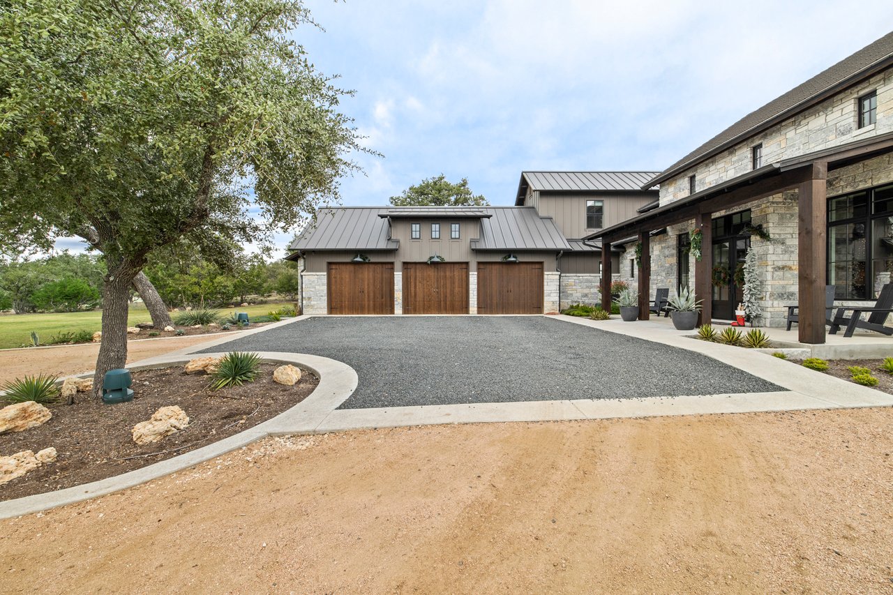 Three car garage and motor court framed by oak trees at this Creek Road Ranch home in Dripping Springs, Texas, built by Cody Schmidt Custom Homes.