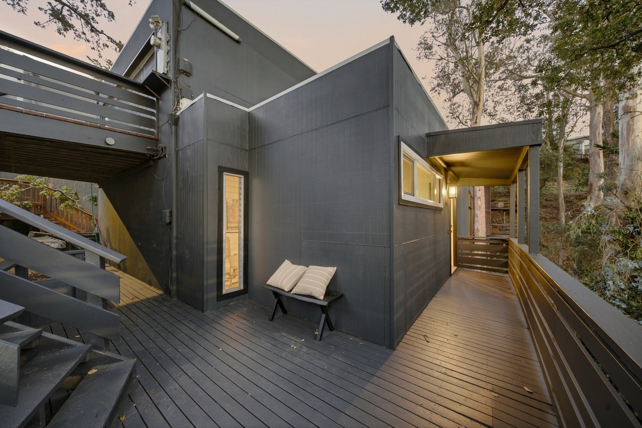 Modern dark-sided home with a wood deck, railings, and a small cushioned bench.