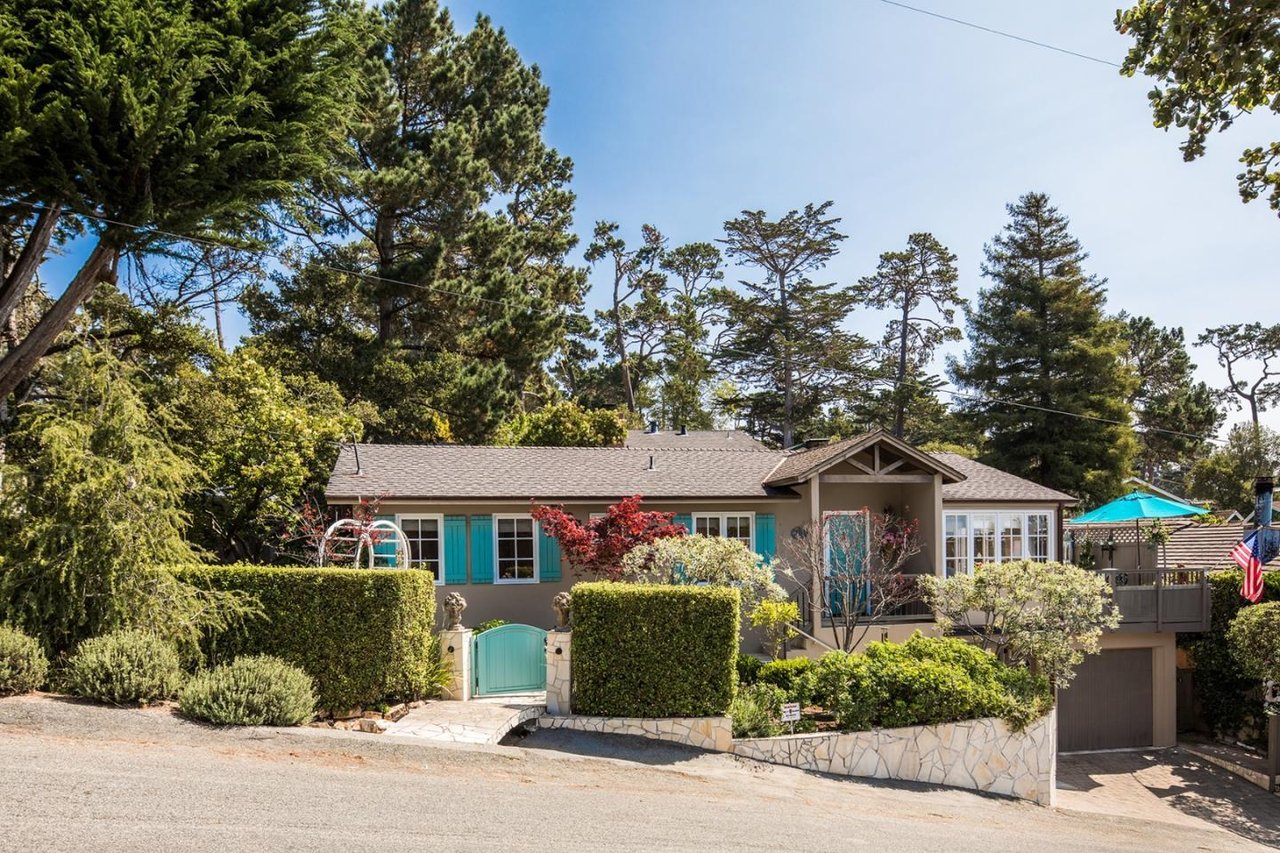 Home with turquoise shutters and gate, landscaped hedges, raised deck, and garage.