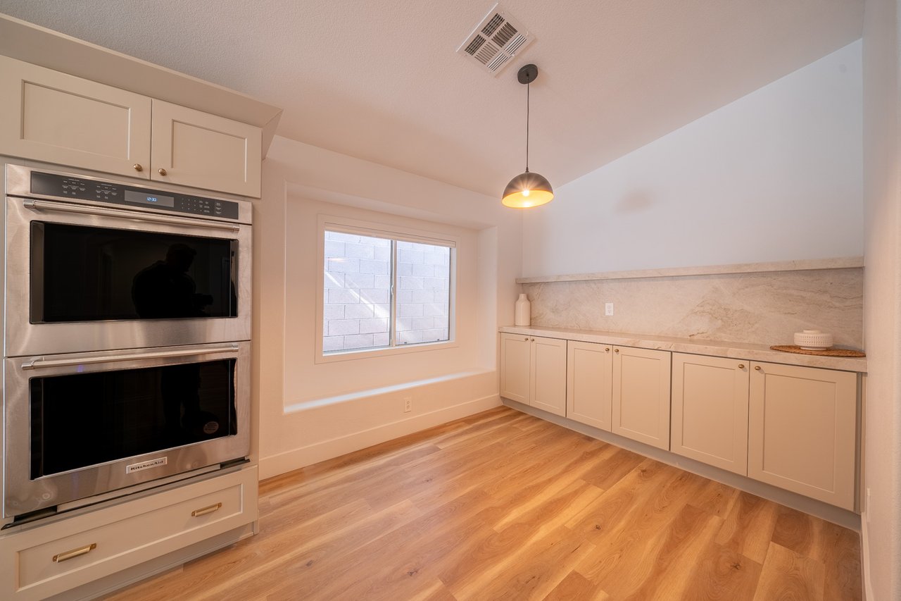 Empty kitchen with a built-in double oven, stone backsplash, and warm wood flooring.