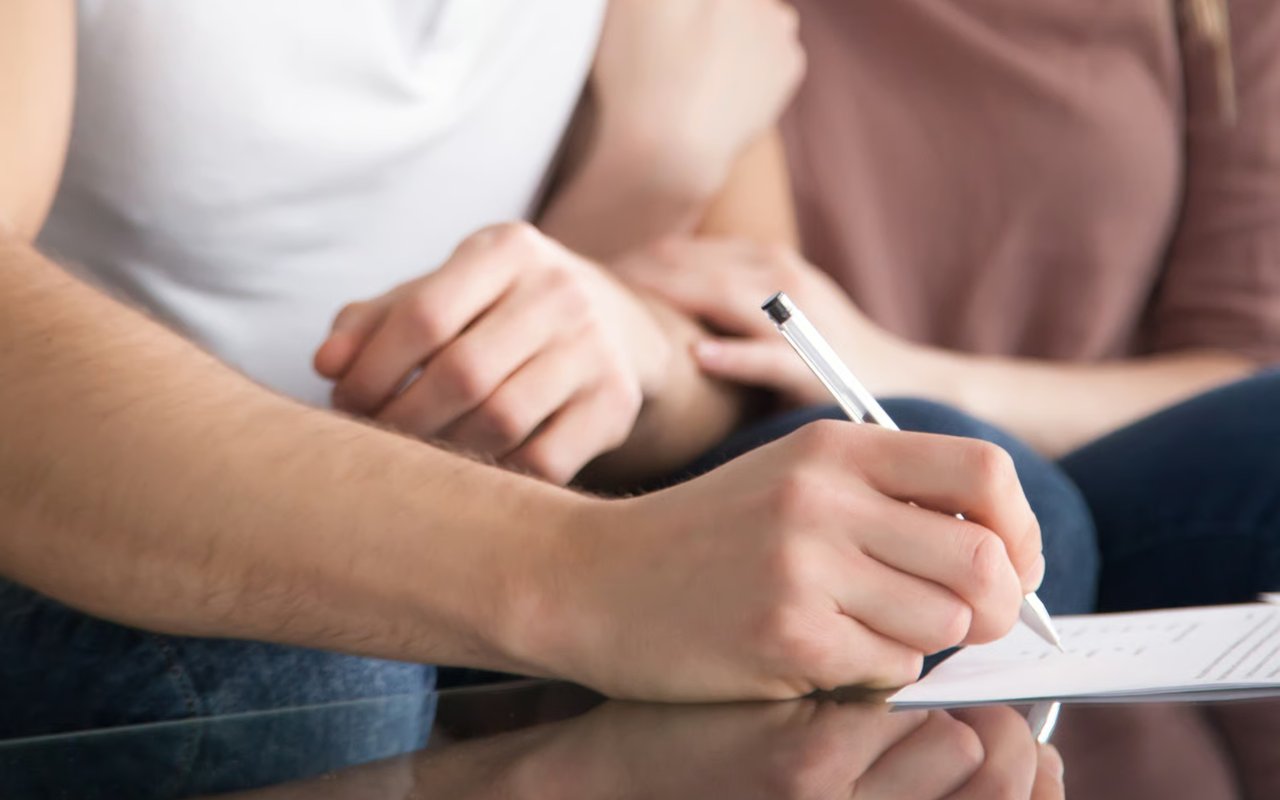 A close-up of two people signing documents with a pen, representing the closing of sales and escrows.