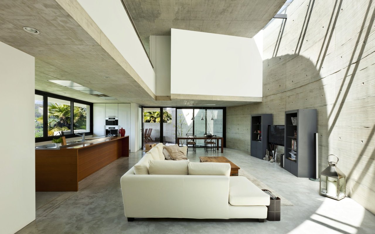 Open-plan living room with a white sectional, wood kitchen island, and exposed concrete walls.