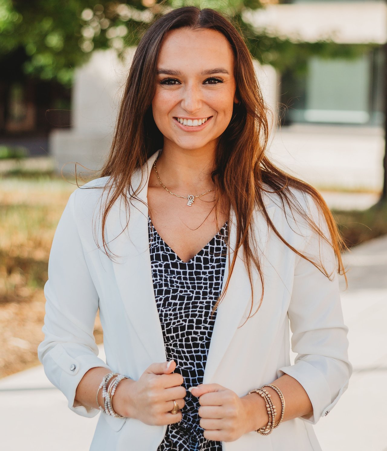 Emma Garcia smiling in a white blazer over a patterned top outdoors.