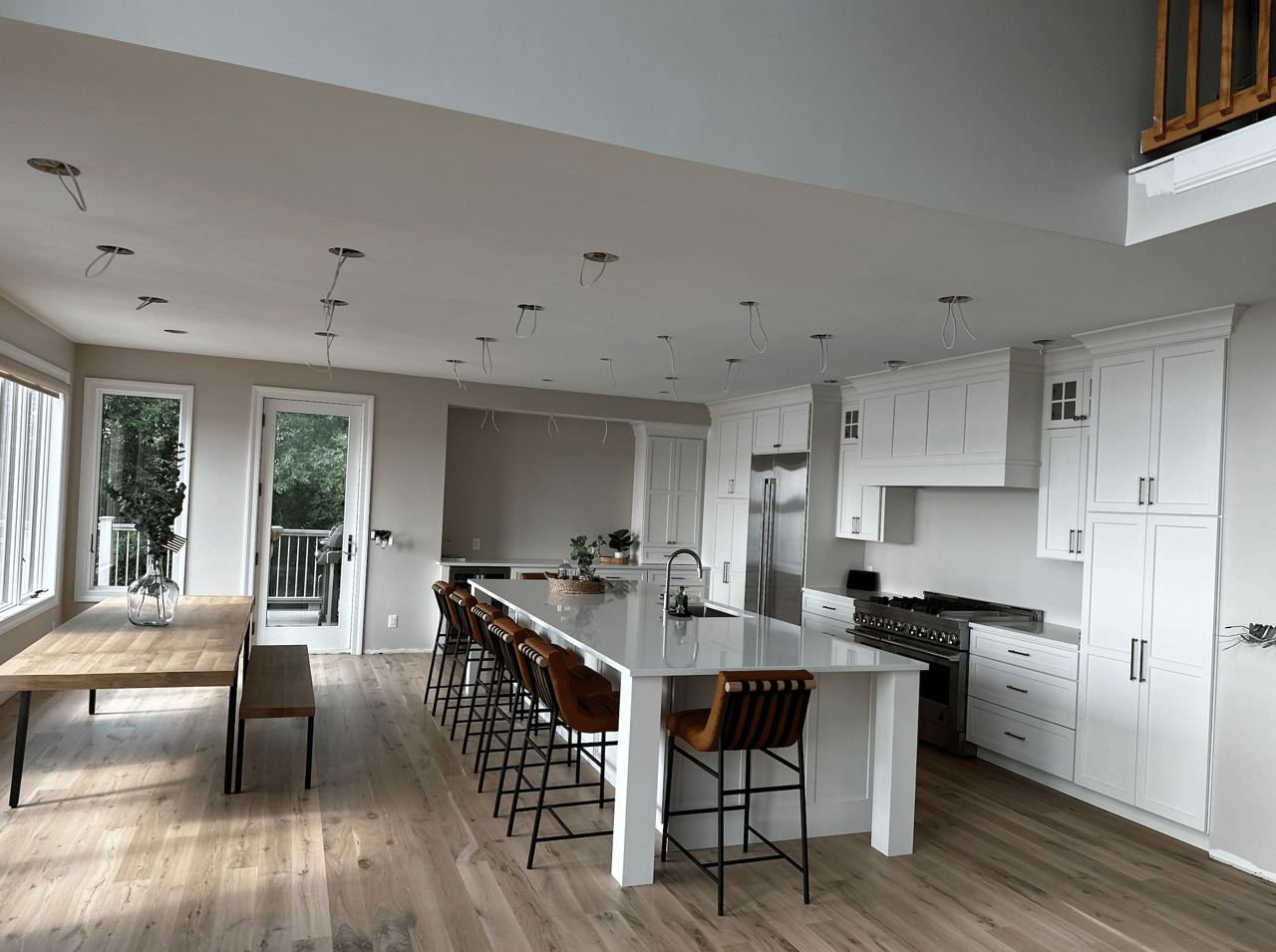 Open-plan kitchen with a large island, brown bar stools, white cabinets, and unfinished ceiling lights.