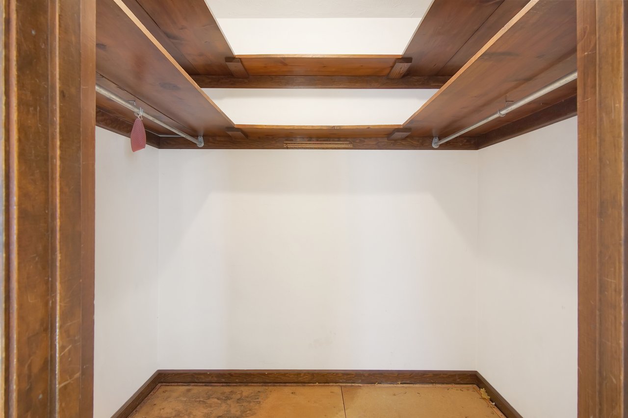 Empty closet with white walls and wooden shelves, featuring a hanging rod with a single small item. The space appears clean and minimal.