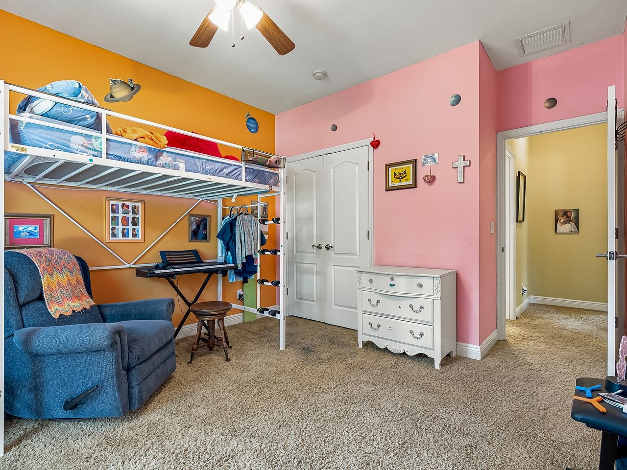 Bedroom with a raised bunk bed, blue recliner, and colorful orange and pink walls.