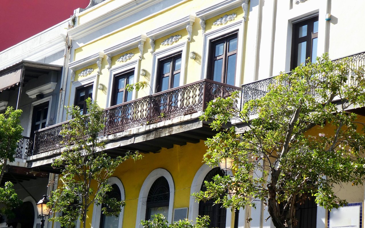 Yellow-and-white building with ornate iron balconies, tall windows, and arched ground-floor windows.