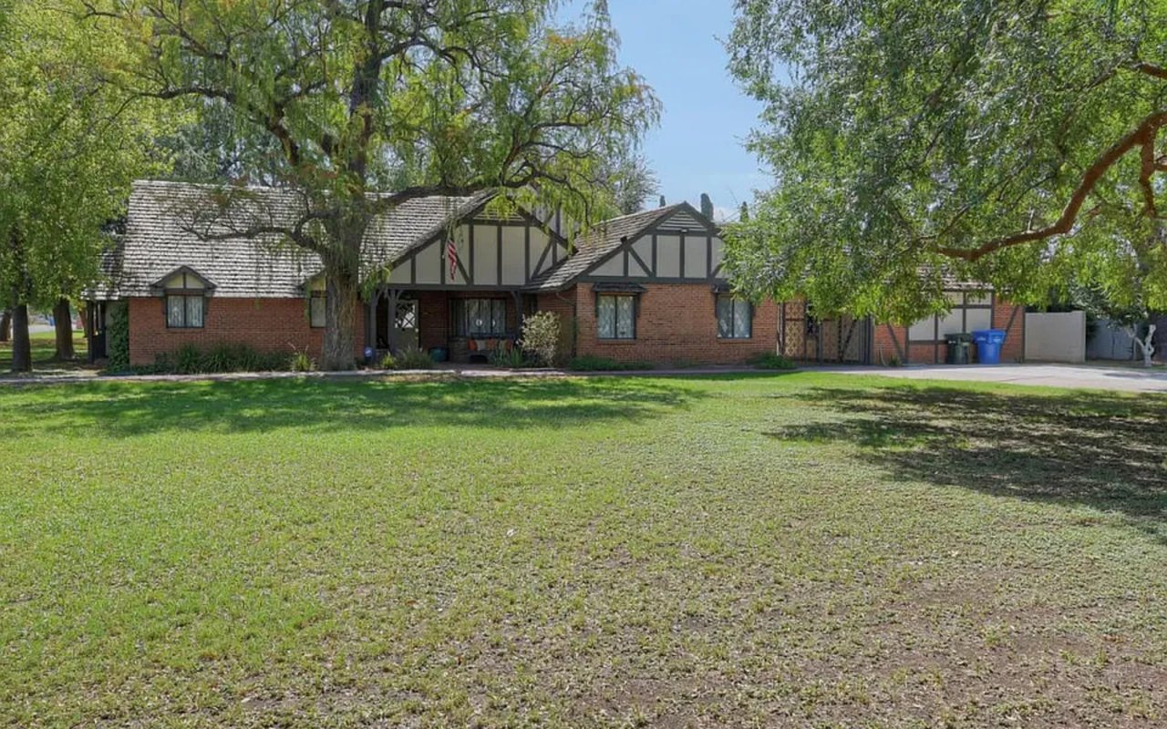 Brick house with timbered gables, mature trees, and a broad front lawn.