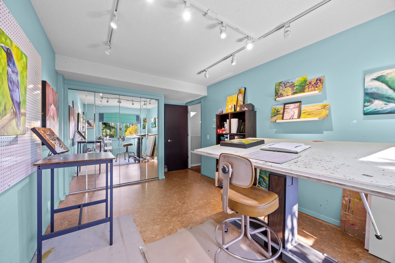 Art studio with turquoise walls, displayed paintings, and large drafting tables.