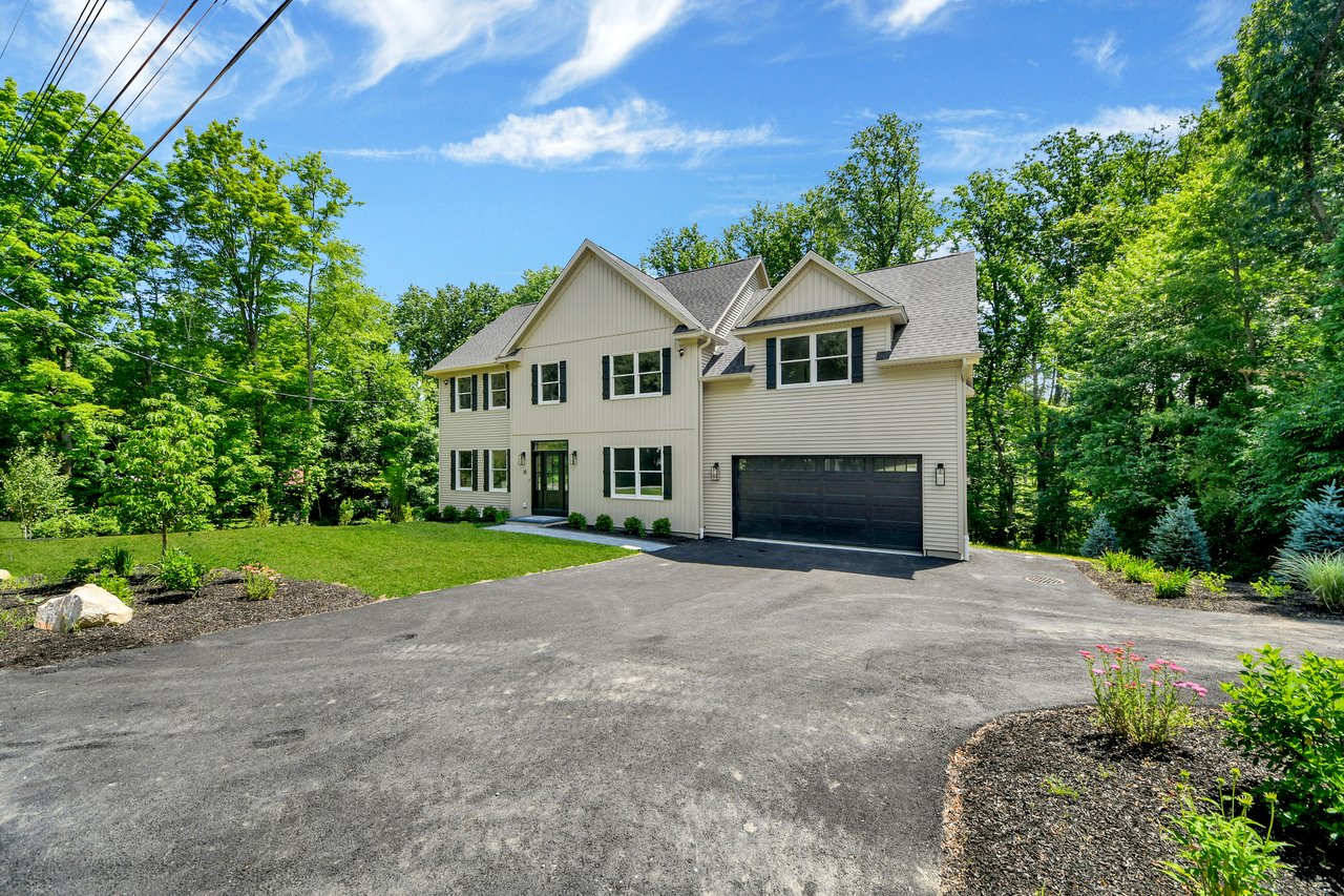 Two-story light-colored house with a dark garage, broad driveway, and leafy landscaped yard.