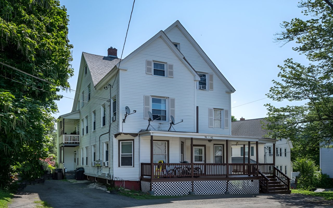White multi-story clapboard building with a long covered porch and lattice skirting.