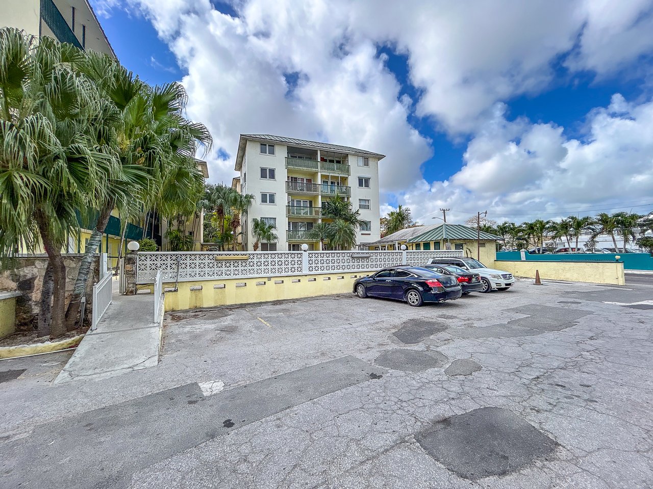 Apartment building with balconies, palm trees, and a parking area in front.