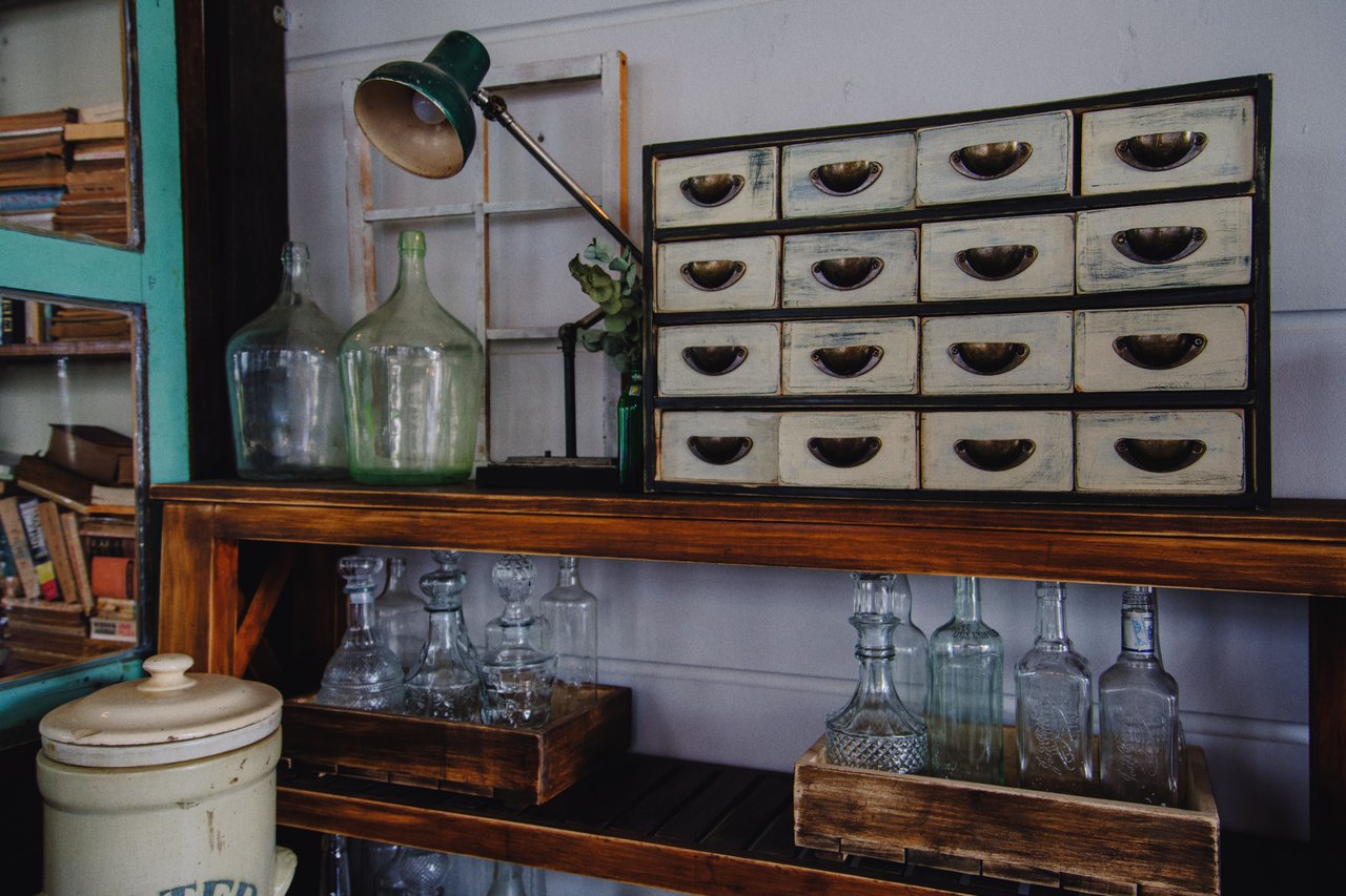 Vintage shop display with a distressed drawer cabinet, green glass bottles, and antique glassware.