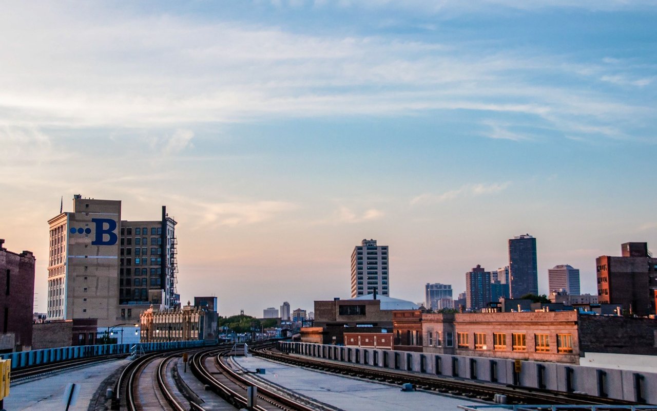 Chicago skyline and elevated train tracks at sunset, with a large B sign on a nearby building.