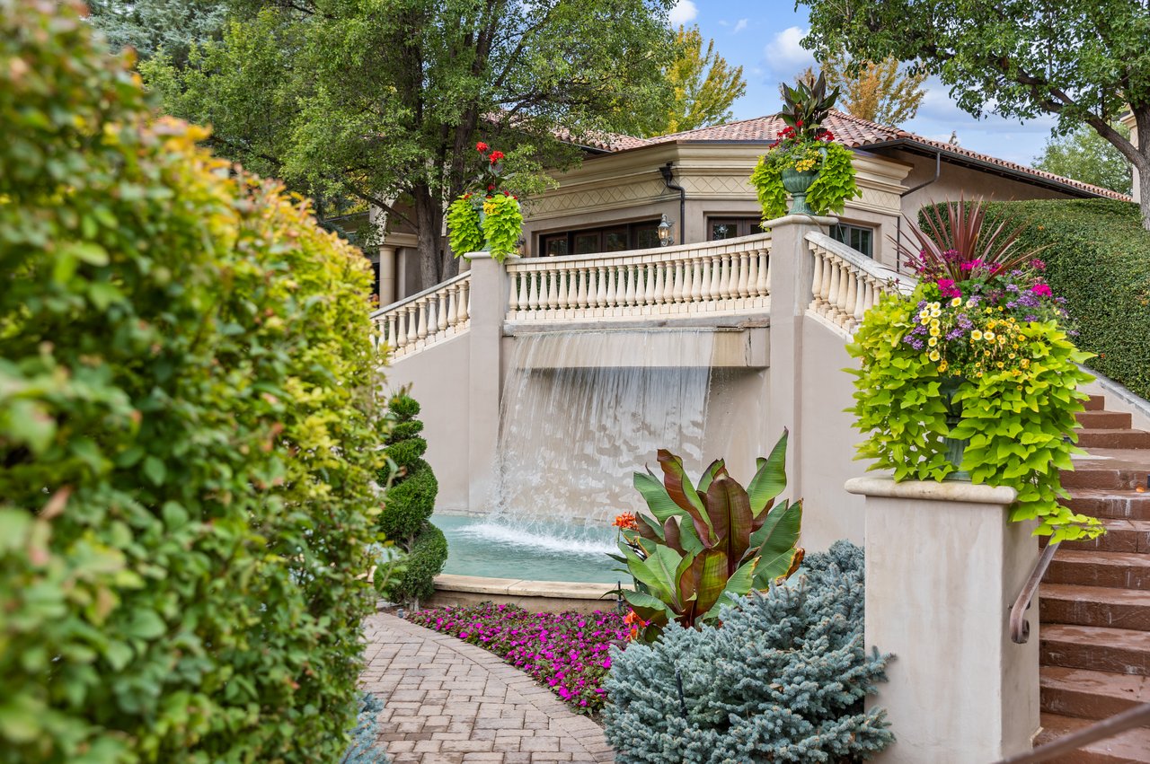 Estate garden with a cascading waterfall, flowering planters, and stone steps.