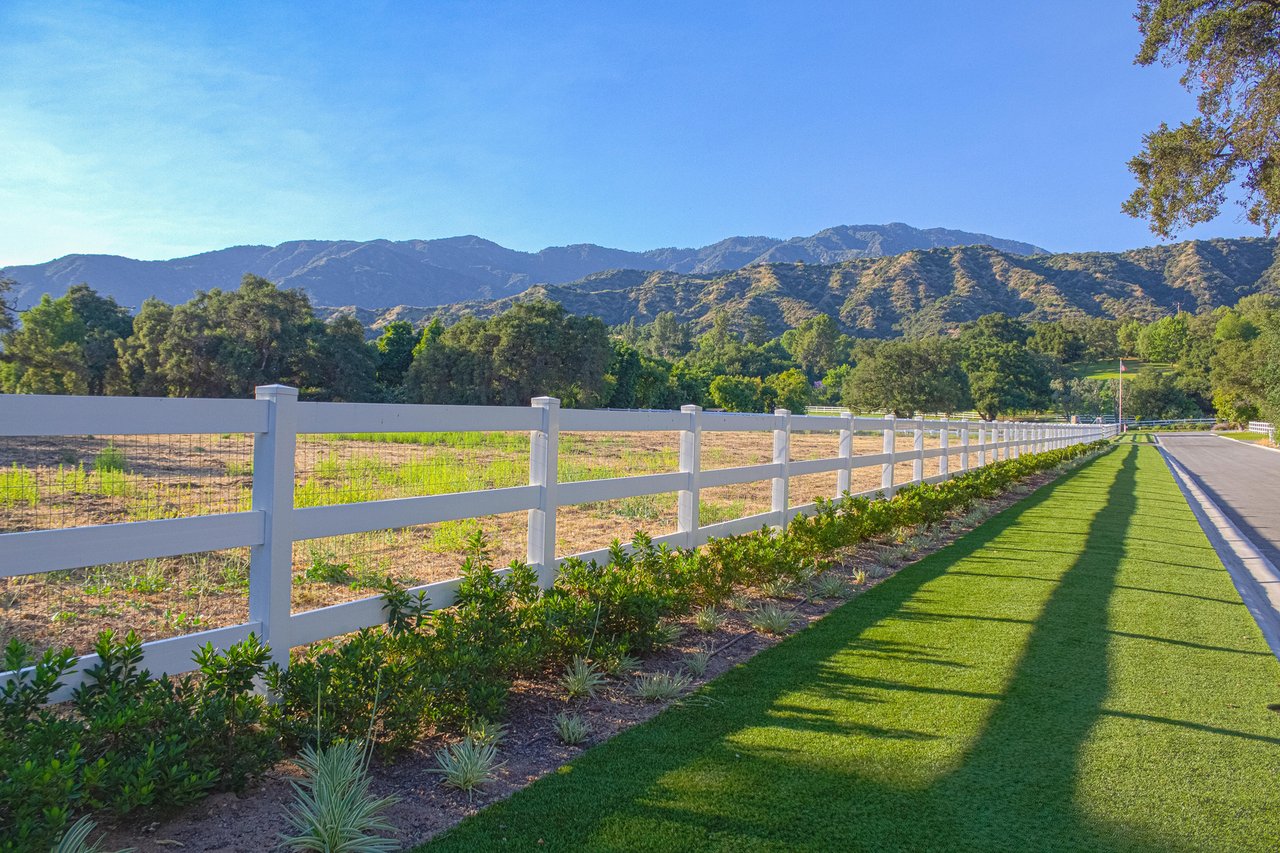 White estate fencing along a Bradbury road with open grounds and the San Gabriel foothills beyond