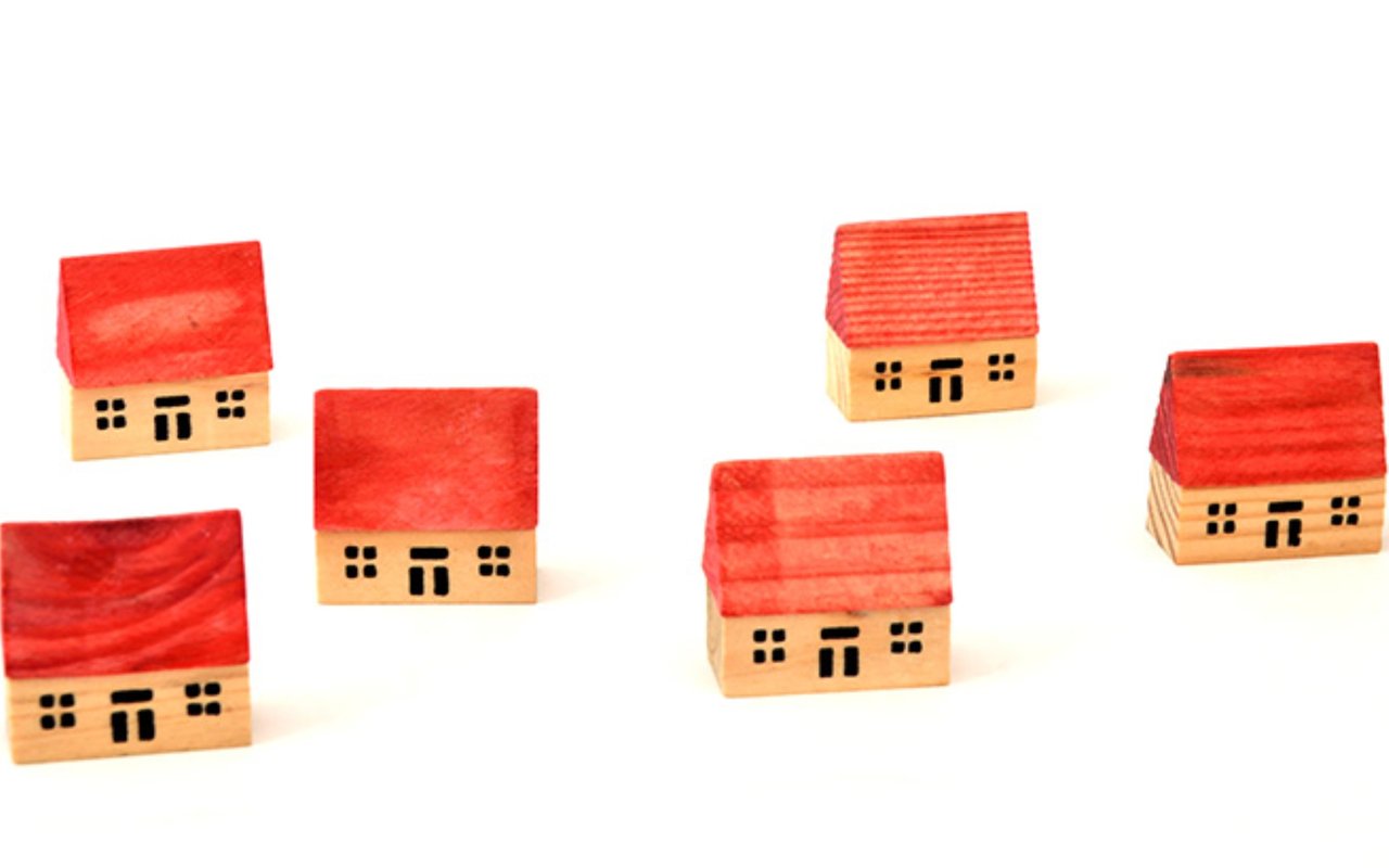 Five wooden model houses with bright red roofs arranged on a white surface.