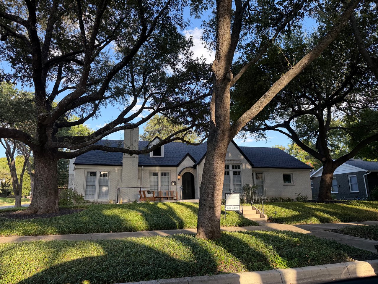 Light brick Ryan Place home with an arched entry, broad steps, and mature oak trees.