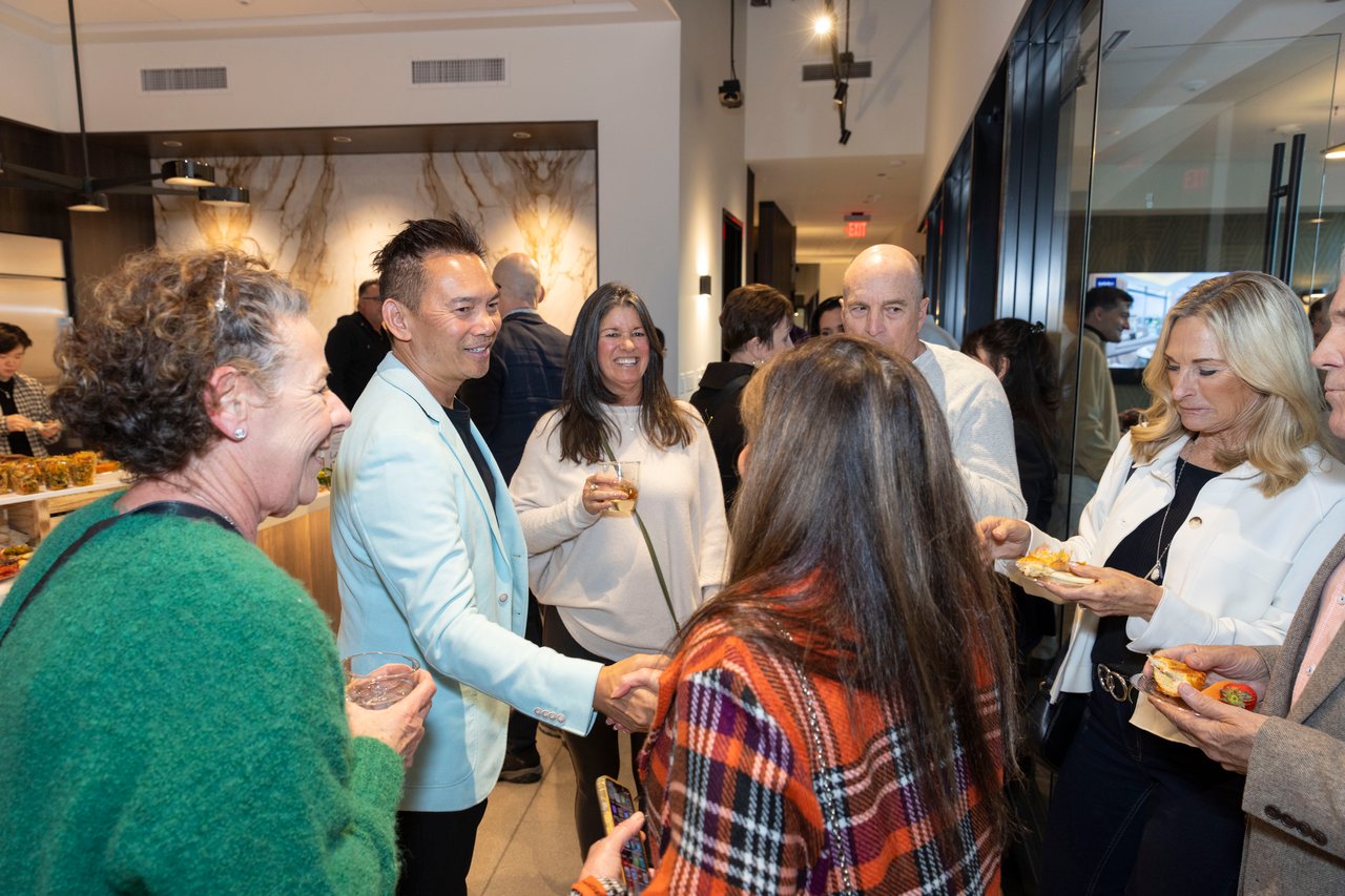 Guests mingle at an indoor open house, with refreshments and a marble-patterned wall nearby.