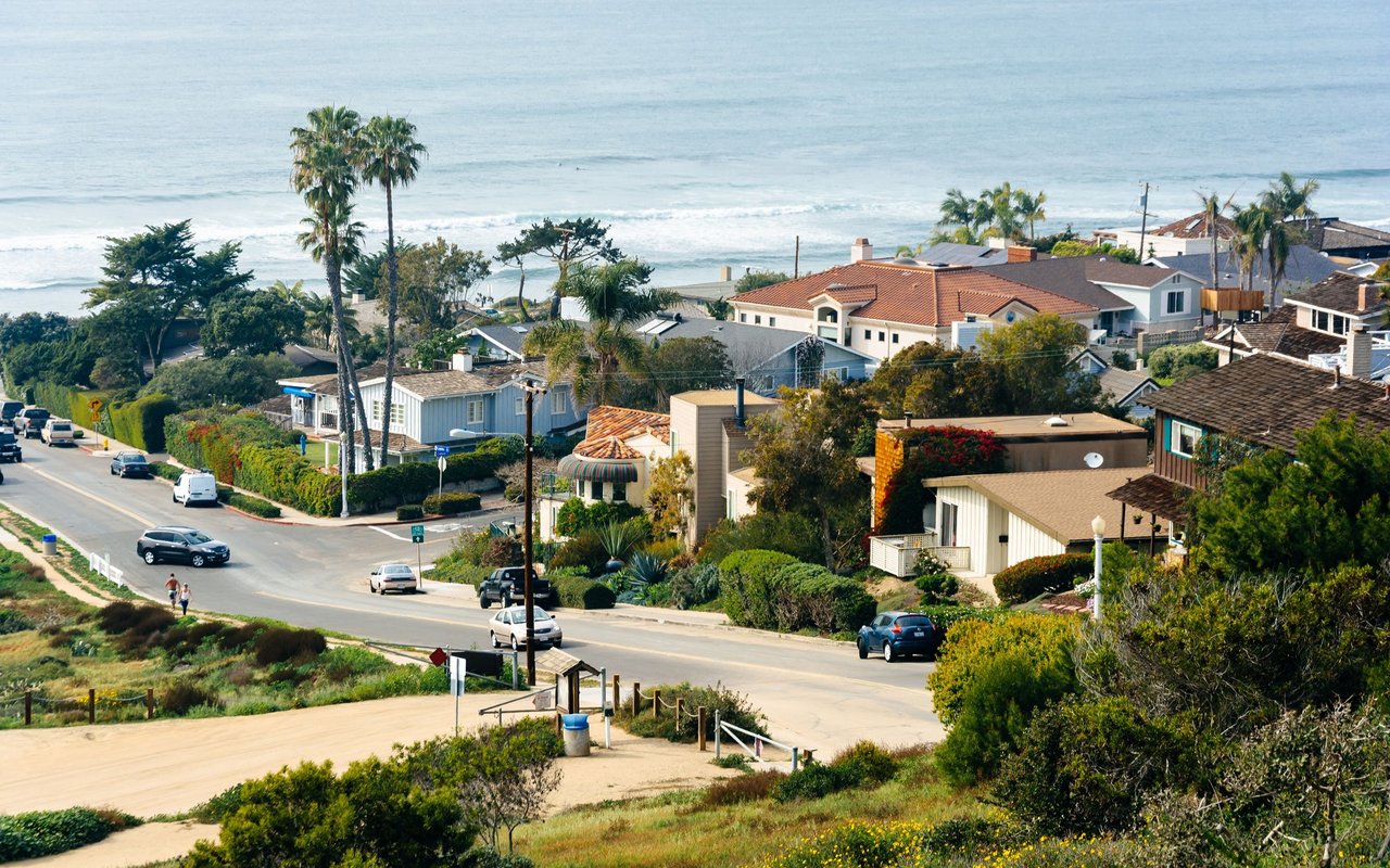 Coastal neighborhood with palm-lined homes, a road, and oceanfront beach.