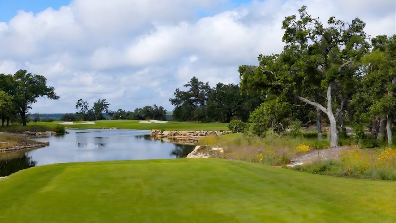 Tee box overlooking a golf hole with water feature, stone edge, and oak trees at Maverick Golf & Ranch Club in Fort Worth, Texas.