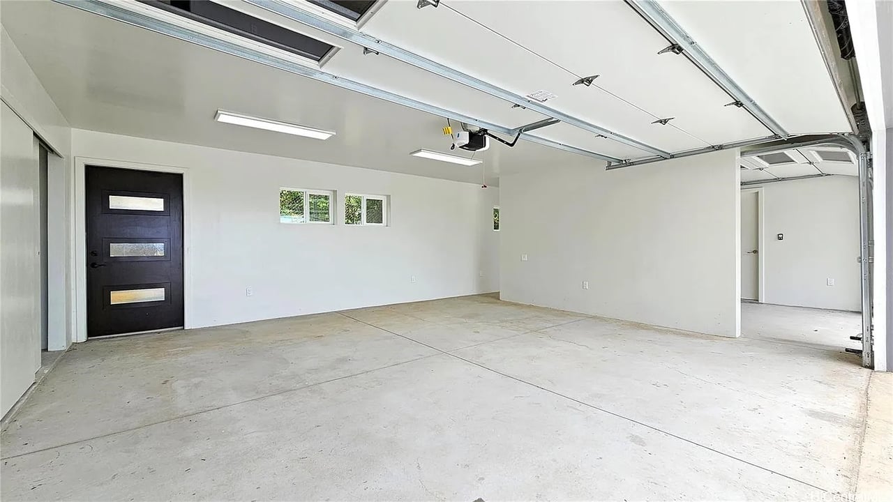 Vacant garage with a concrete floor, overhead doors, and a black side entrance door.