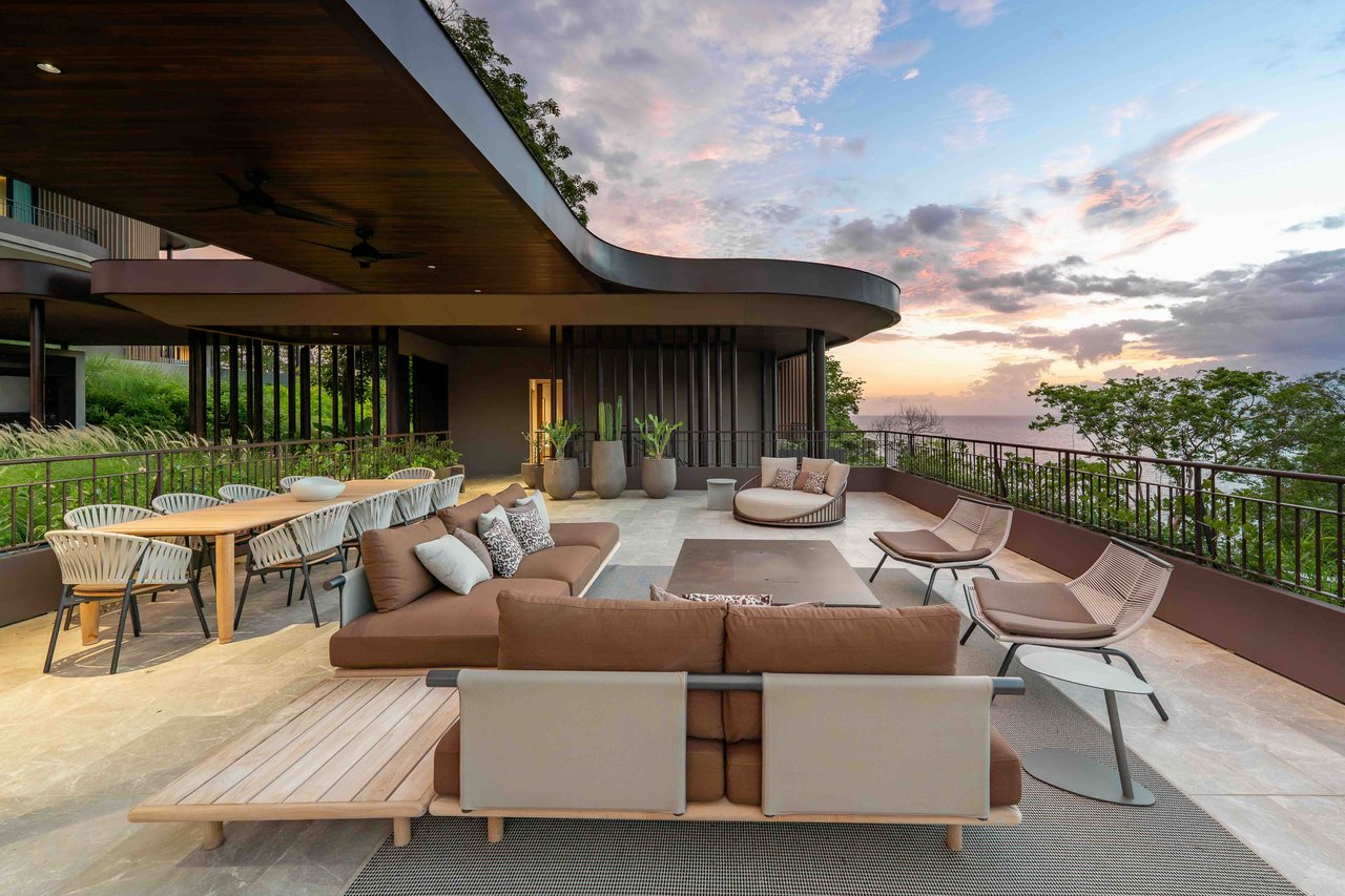 Furnished ocean-view terrace with a curved roof, outdoor dining area, and lounge seating at sunset.