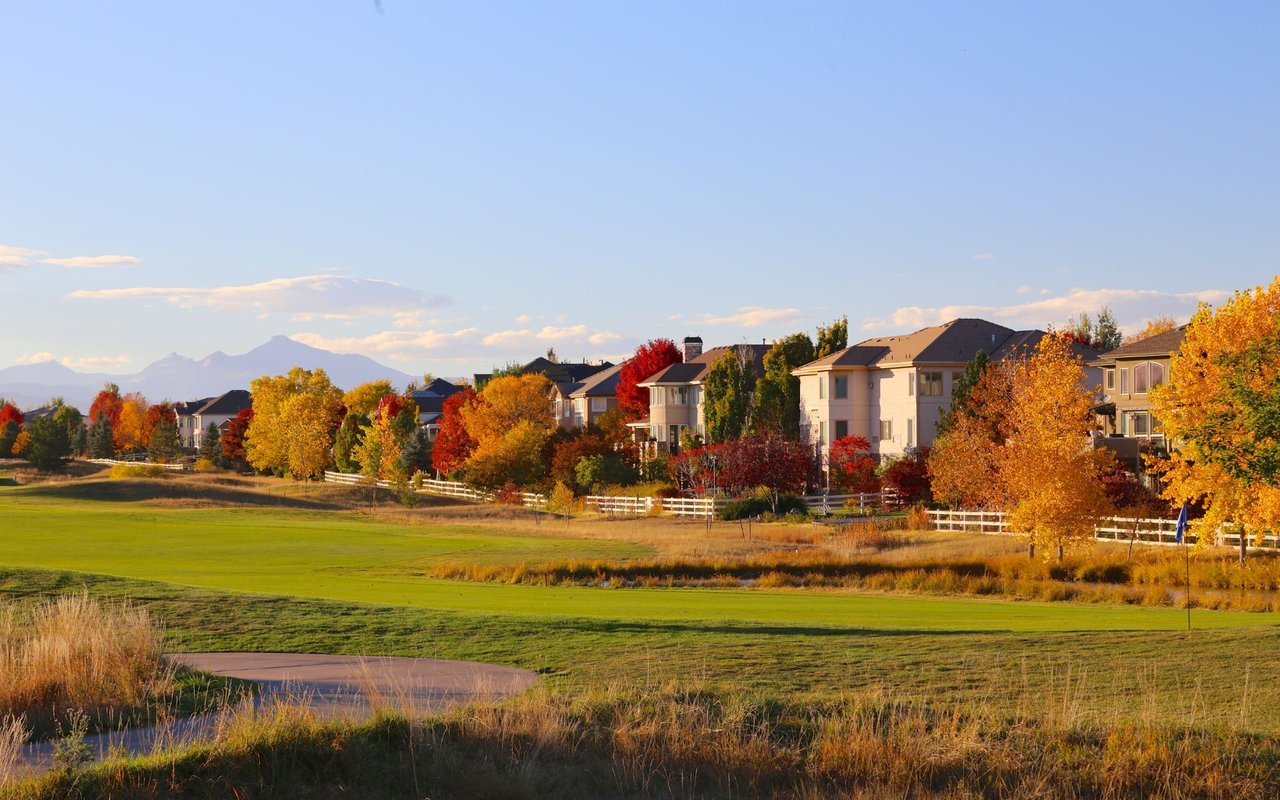 Suburban homes along a golf course, framed by colorful autumn trees and distant mountains.