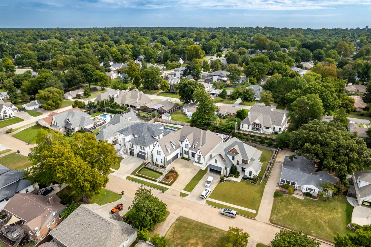 Aerial view of white homes with gray roofs amid a leafy residential neighborhood.