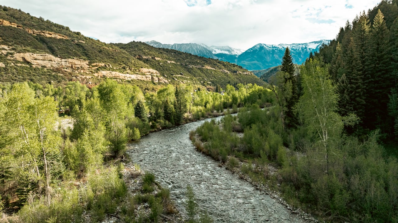 River winding through a wooded mountain valley with snow-capped peaks beyond.