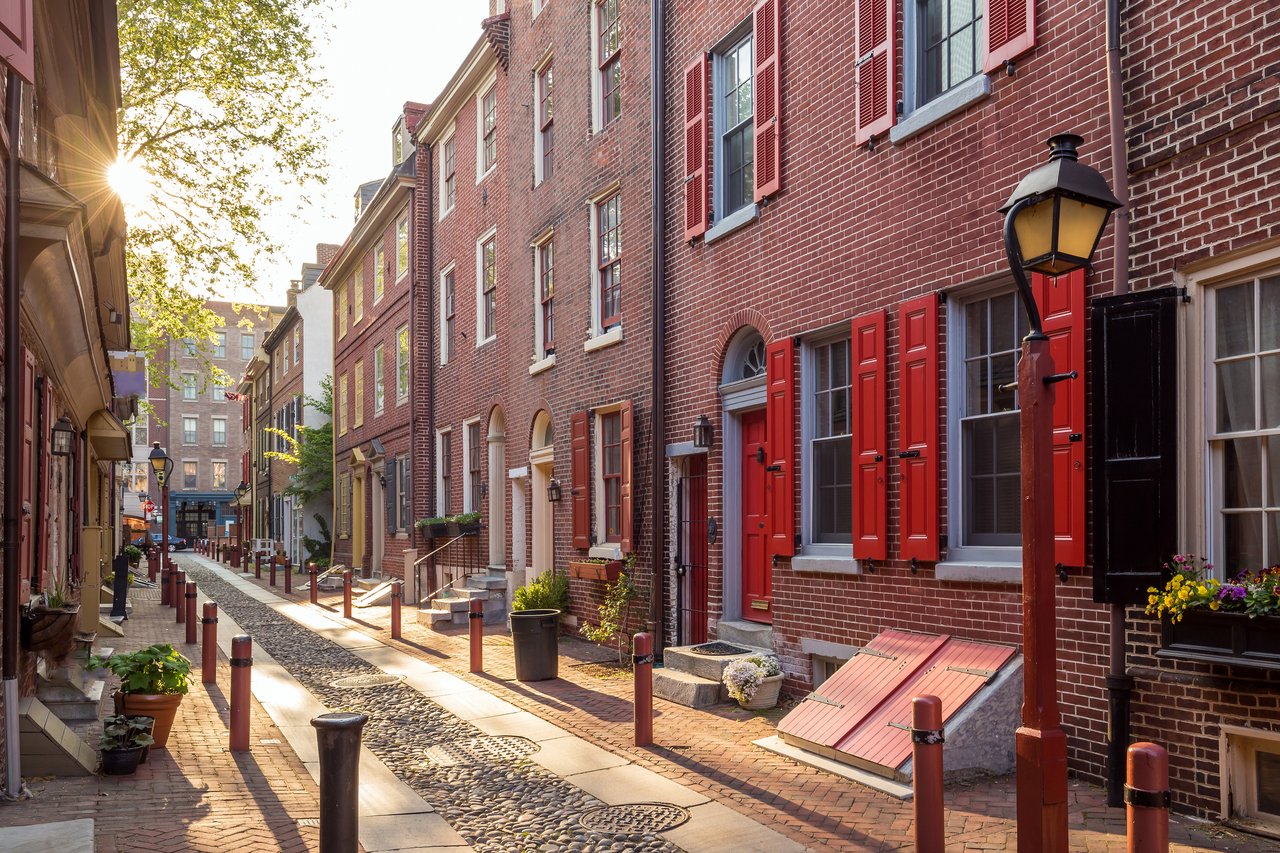 Old City cobblestone lane lined with historic brick rowhouses and red shutters.
