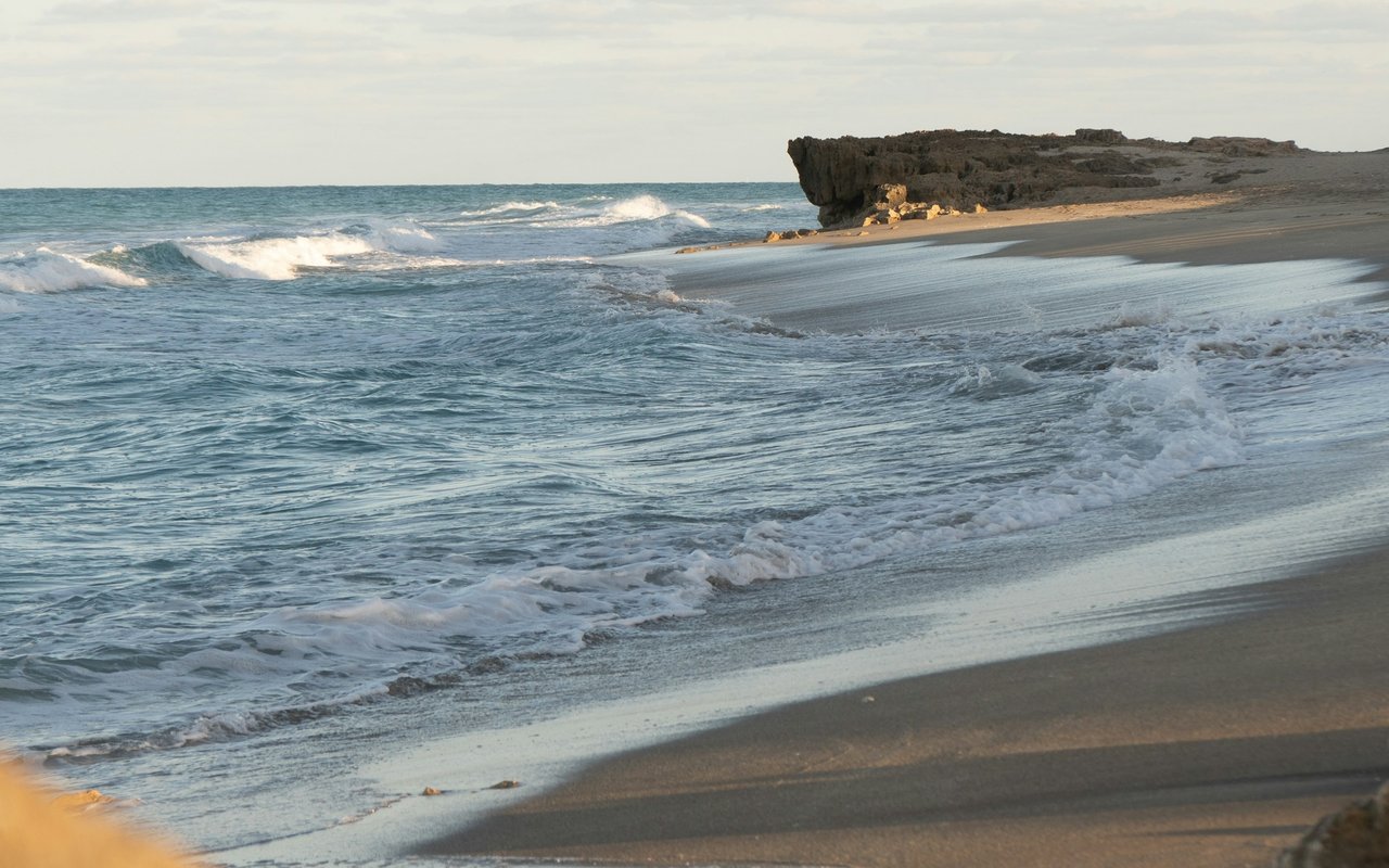 Waves wash onto wet sand beside a low rocky outcrop.