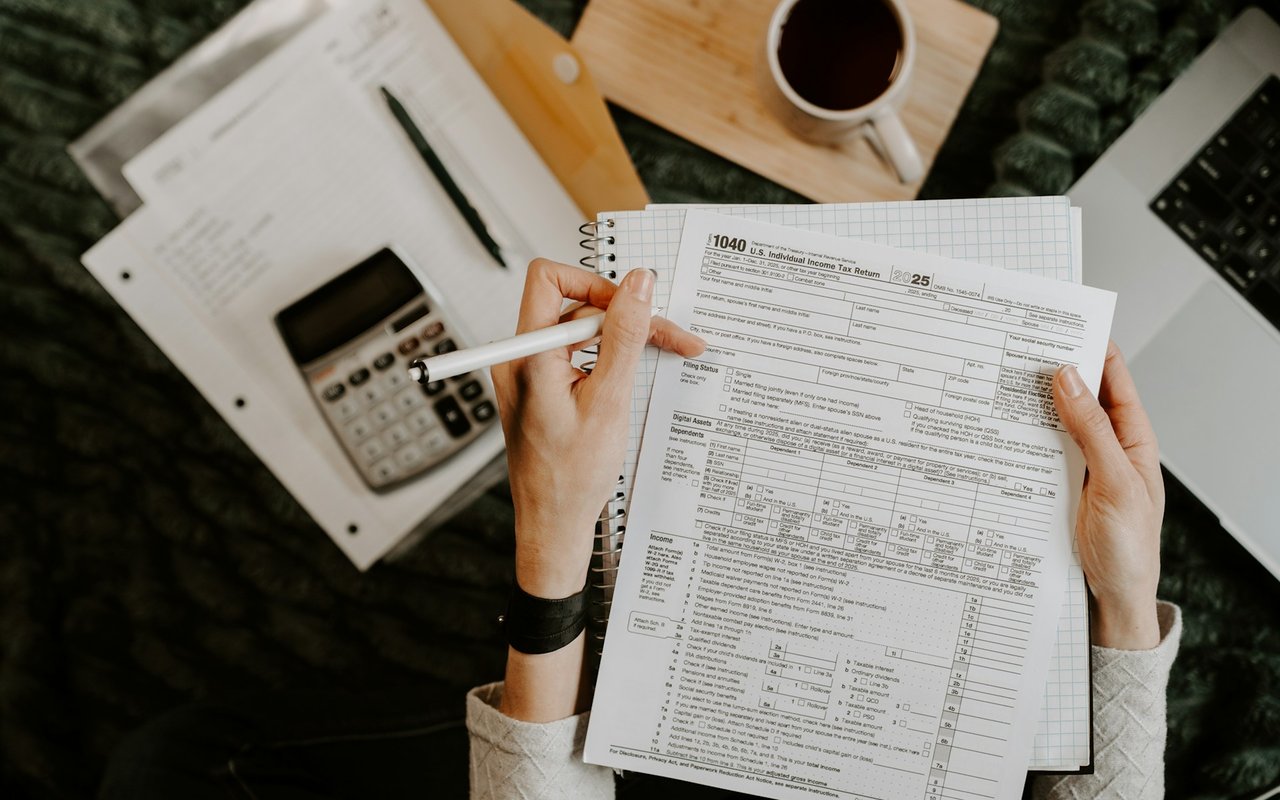 Hands review a 2025 tax return beside a calculator, notebook, and coffee.