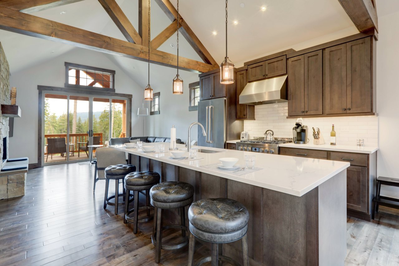 Kitchen with a large white island, dark wood cabinets, exposed beams, and sliding doors to a wooded view.