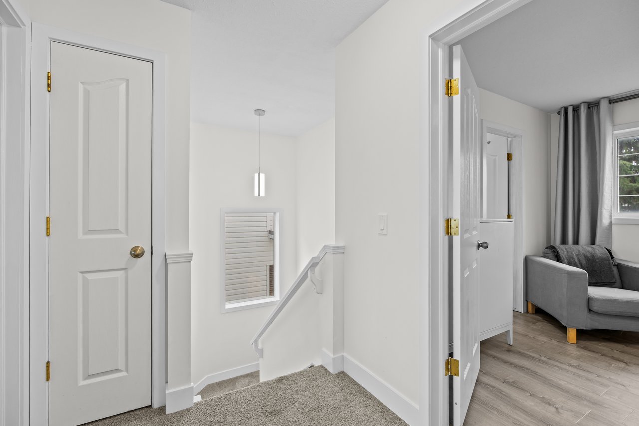 Upstairs hallway and stair landing with white paneled doors and a view into a living room.