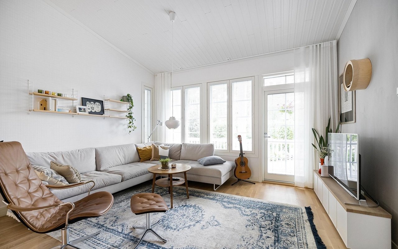 Bright living room with a white sectional, leather lounge chair, patterned rug, and tall balcony windows.