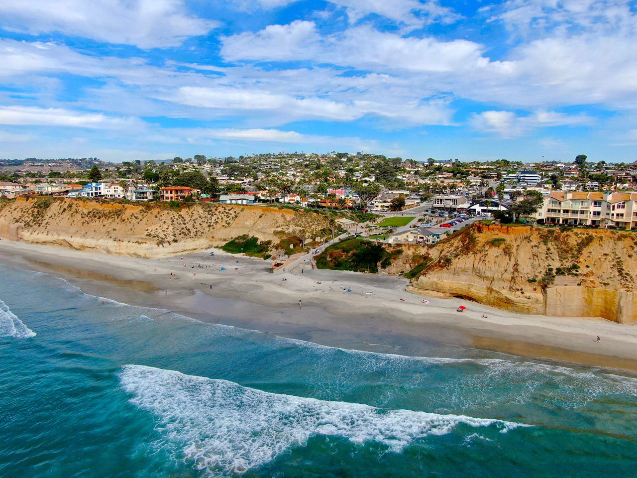 Coastal neighborhood on sandy bluffs above a beach and turquoise ocean.