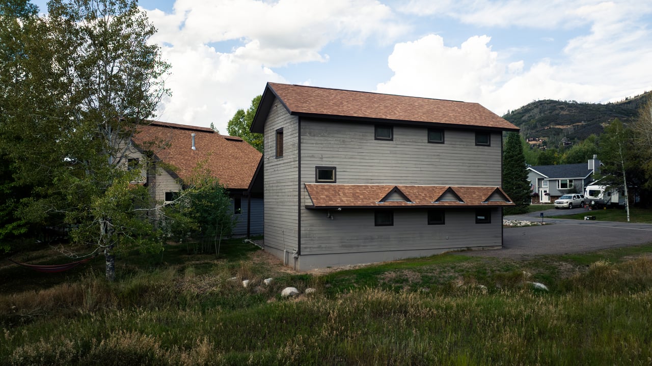 Two gray-sided Meadow Lane buildings with brown roofs, backed by trees and a mountain.